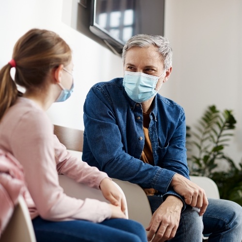 Two people wearing face masks sitting in dental office waiting area