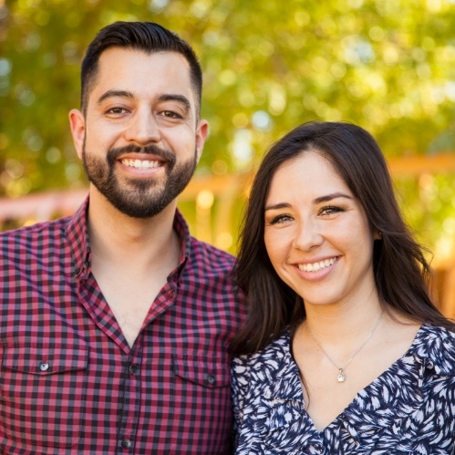 Man and woman smiling outdoors with green trees in background