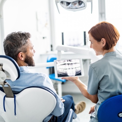 Dentist showing tablet with x rays of teeth to a patient in dental chair