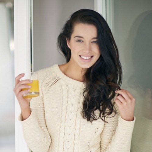 Smiling woman in white sweater holding a glass of orange juice