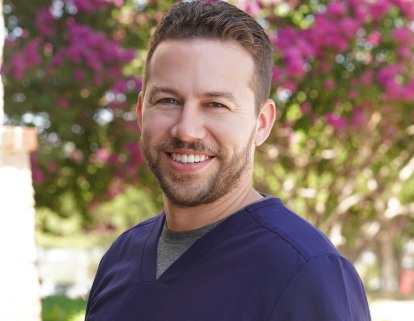 Carrollton dentist Doctor Jordan smiling in dark blue scrubs