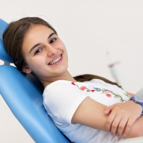 Smiling teenage girl with braces leaning back in dental chair