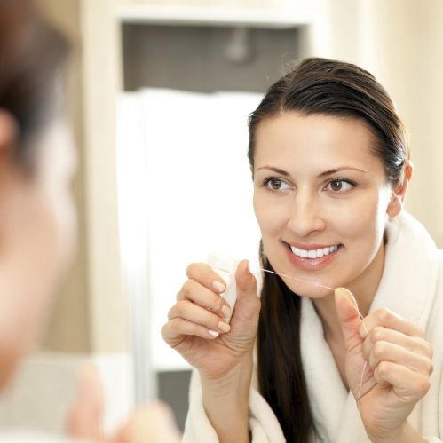 Woman flossing her teeth in front of bathroom mirror