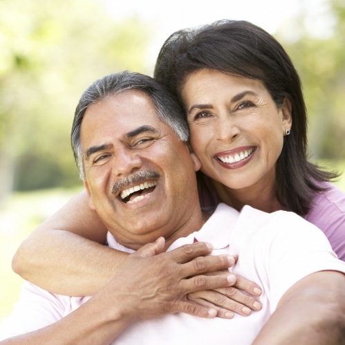 Older man and woman hugging outdoors after preventive dentistry in Carrollton
