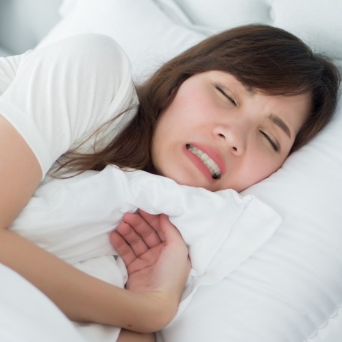 Woman wincing in pain while laying in bed
