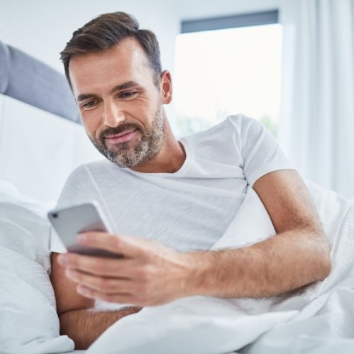 Man laying in bed and smiling at his phone