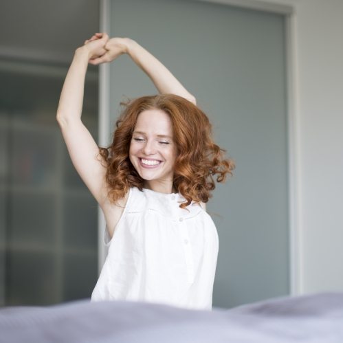 Woman grinning and stretching while sitting up in bed