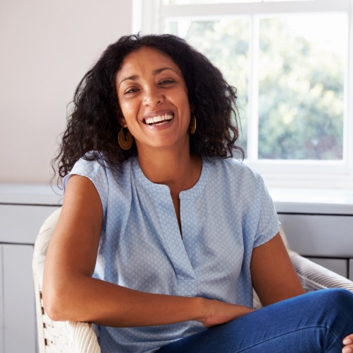 Woman smiling in armchair after tooth replacement in Carrollton