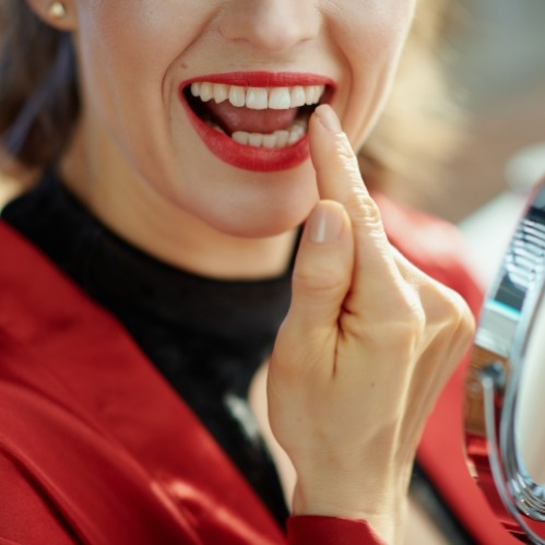 Woman with red lipstick looking at her teeth in mirror