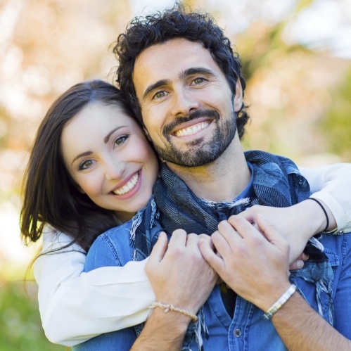 Smiling woman hugging man from behind outdoors